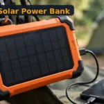 BLAVOR Solar Power Bank Review: 20000mAh, 4 Built-In Cables and an Apple Watch Charger — With One Big Solar Catch (2026) BLAVOR solar power bank review - orange 20000mAh solar charger with built-in cables at a sunny campsite