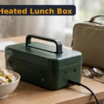 Buddew electric lunch box review - heated lunch box with steaming hot food beside its carry bag on an office desk